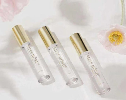 Three clear rollerball bottles with gold caps on a light background with flowers.